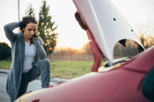 Time to Get Started on Your Summer Maintenance Checklist with C's Autohaus in Centerville Oh, image of woman broke down on side of the road with hood of red car lifted while she has leg leaning on the car using her phone holding the back of her head with her other arm