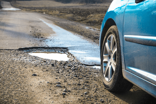 Hit a Pothole Hard? Visit Our Auto Repair Shop in Centerville OH with C's Autohaus image of teal car driving toward big pothole in road