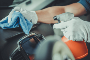 Keep Germs at Bay with PermaSafe Vehicle Disinfection with C's Autohaus in Centerville Oh; image of mechanic using permasafe disinfectant on dash of vehicle near steering wheel in shop while wearing protective gloves