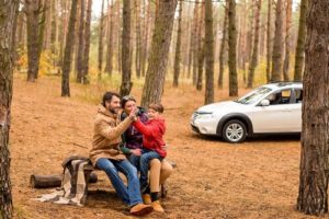 Fall Car Care for Euros, Exotics, and Luxury Cars with C's Autohaus in Dayton, OH; image of happy family on bench in the woods during fall with their white subaru car in the background