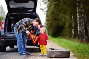 Why Do Pre-Trip Inspections Before You Head Out | C's Autohaus in Centerville, OH. Image of a father and his little son on a summer day waiting for car repair on the roadside. With dark-blue car in the background.