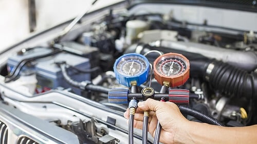 The Summer Heat Is On But Why Is My Car AC Not Blowing Cold Air? | C’s Autohaus in Centerville, OH. Image of a mechanic’s hand detecting refrigerant leak with manifold gauge.