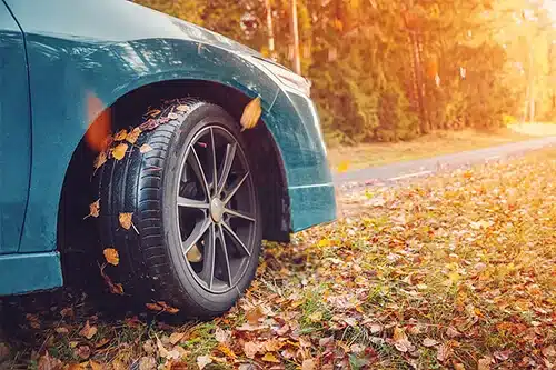 Fall Car Care Tips in Centerville, OH | C’s Autohaus. Closeup image of a blue car on asphalt road in countryside during fall season.