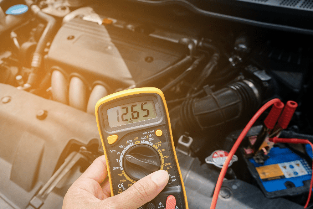 Why fall is the best time to replace your car battery on BMW, Mercedes, Audi and Volkswagens in Centerville, OH. Image of mechanic hand holding battery testing tool while hooked up to car battery in the shop.