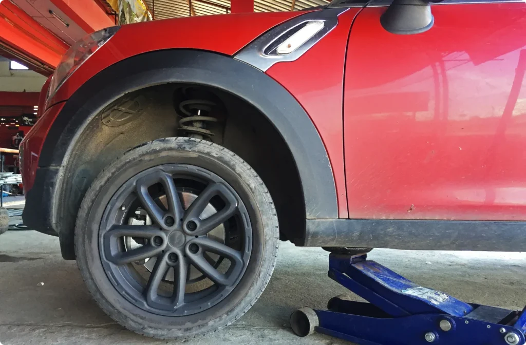 A red Mini Cooper undergoing an auto repair inside an auto repair shop.