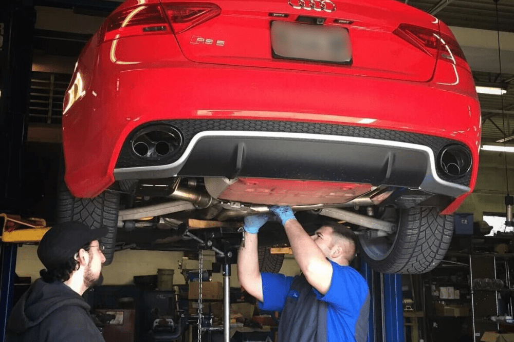 mechanics, auto repair in Centerville, Ohio. C's Autohaus. Mechanics working on the underside of a red Audi lifted in an auto repair shop.