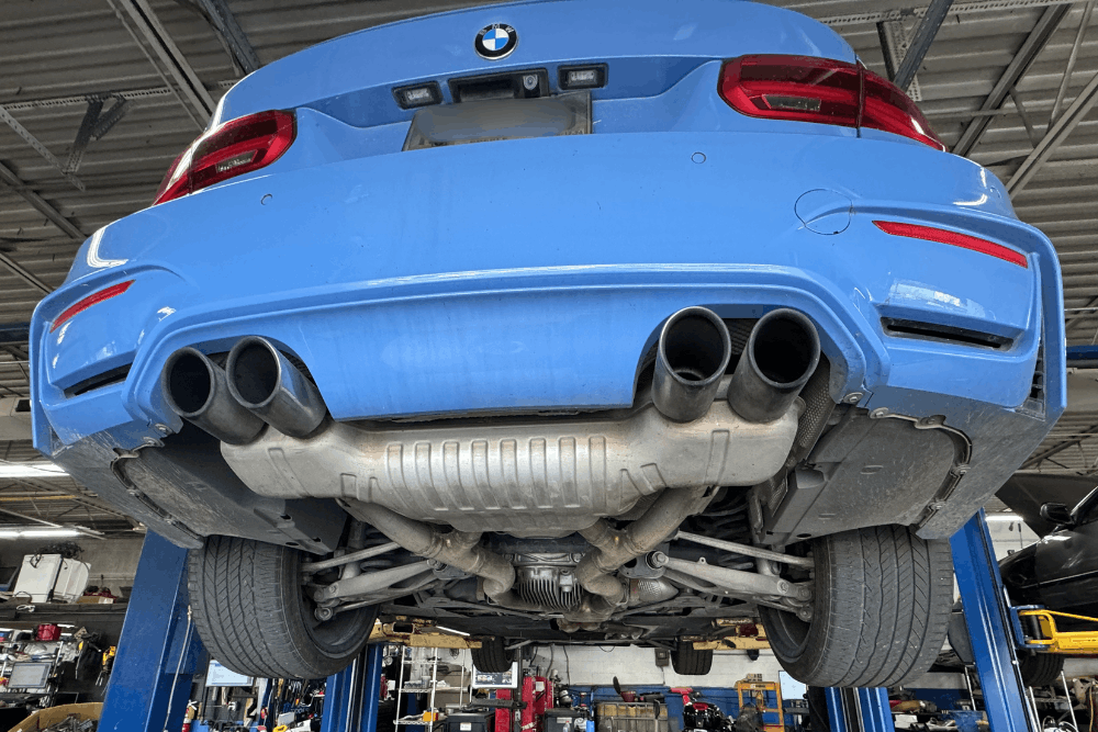BMW repair in Centerville, OH at C's Autohaus. Image of a blue BMW raised on a service lift, showing the rear exhaust and suspension components during inspection and maintenance.