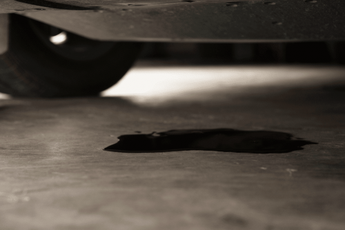 BMW 3 Series oil leak repair in Centerville, OH by C's Autohaus. Image of a dark oil puddle beneath a vehicle, stressing the importance of professional service to protect engine performance and vehicle safety.